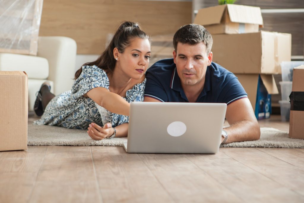 A man and woman are seated on the floor, engaged with a laptop between them